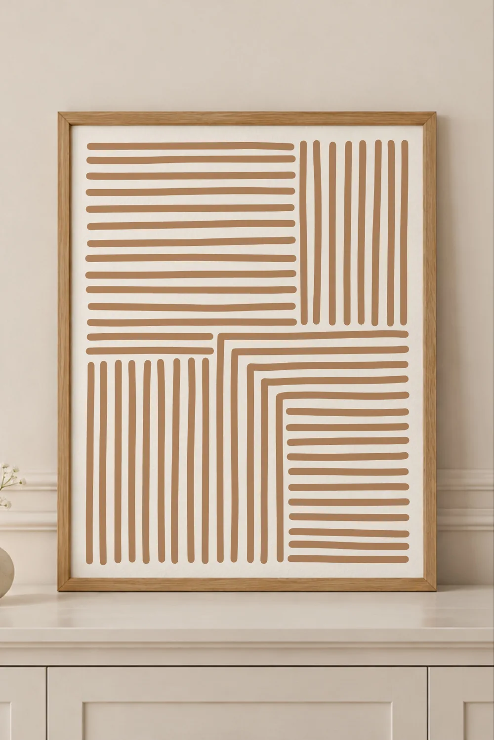 Framed print in a light wood frame on a white cabinet, showing tan abstract line blocks on a cream background