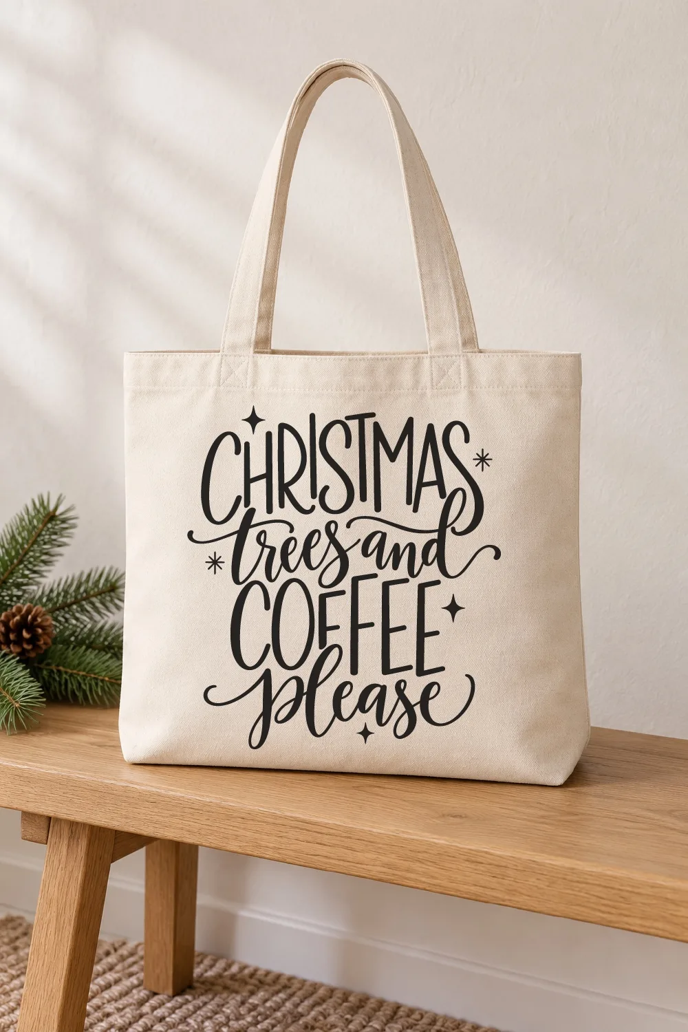 Natural canvas tote bag on a wooden bench beside pine sprigs, with black Christmas Trees and Coffee Please lettering