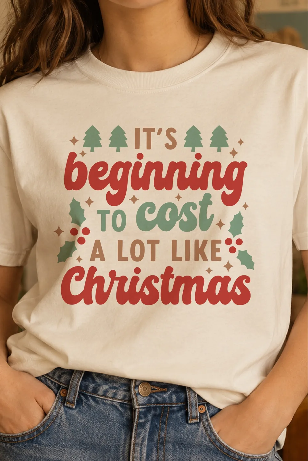 Cream T-shirt worn with jeans showing It's Beginning to Cost a Lot Like Christmas in red, green and tan with trees and holly